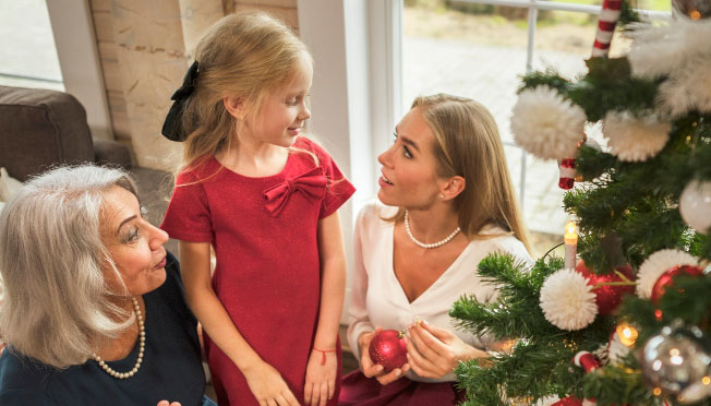 a little girl, her mom and grandma sitting next to the Christmas tree