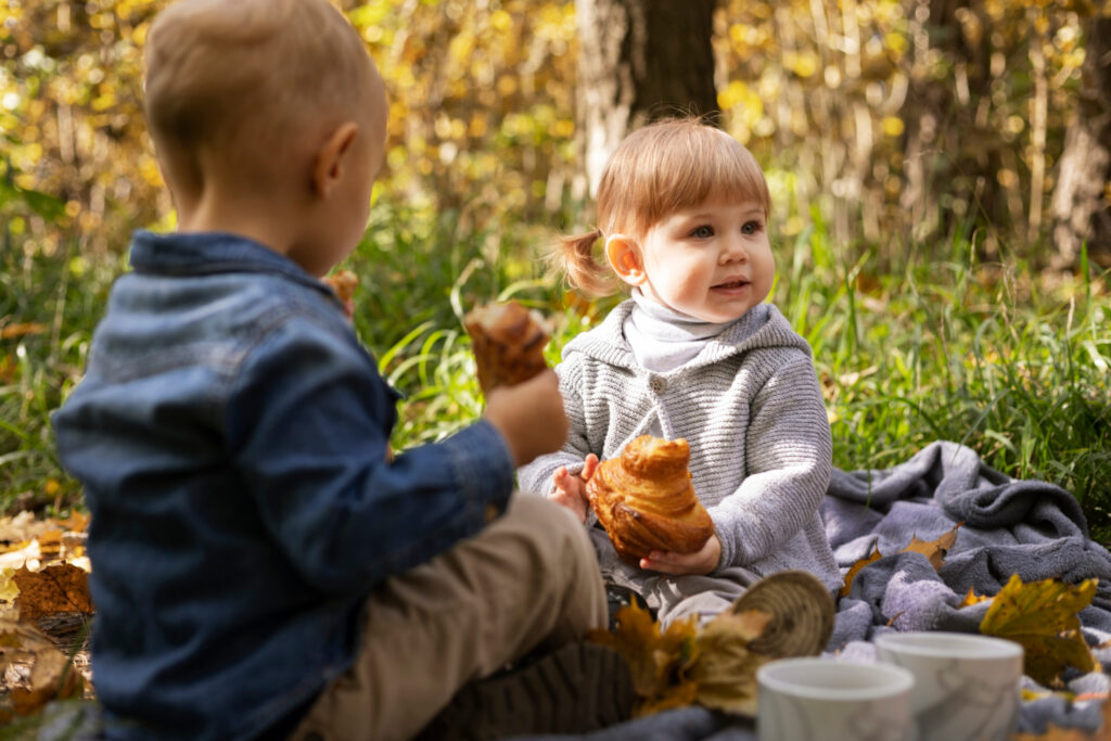 a toddler boy and a small girl sitting on a blanket outside having a picnic