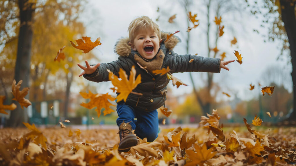 a laughing  toddler boy jumping into fall leaves